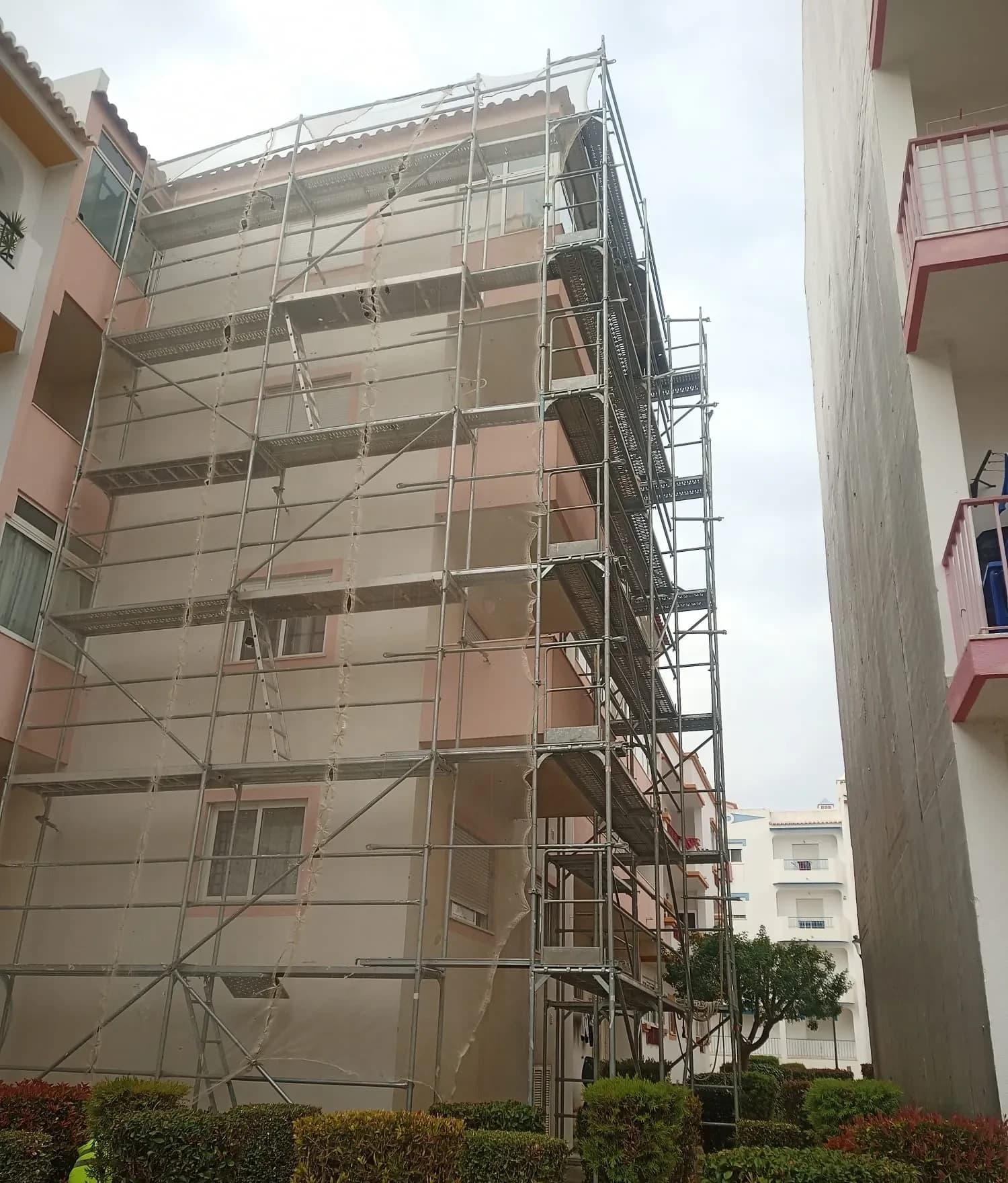 Prédio residencial coberto por andaimes e rede de proteção durante a reabilitação da fachada.